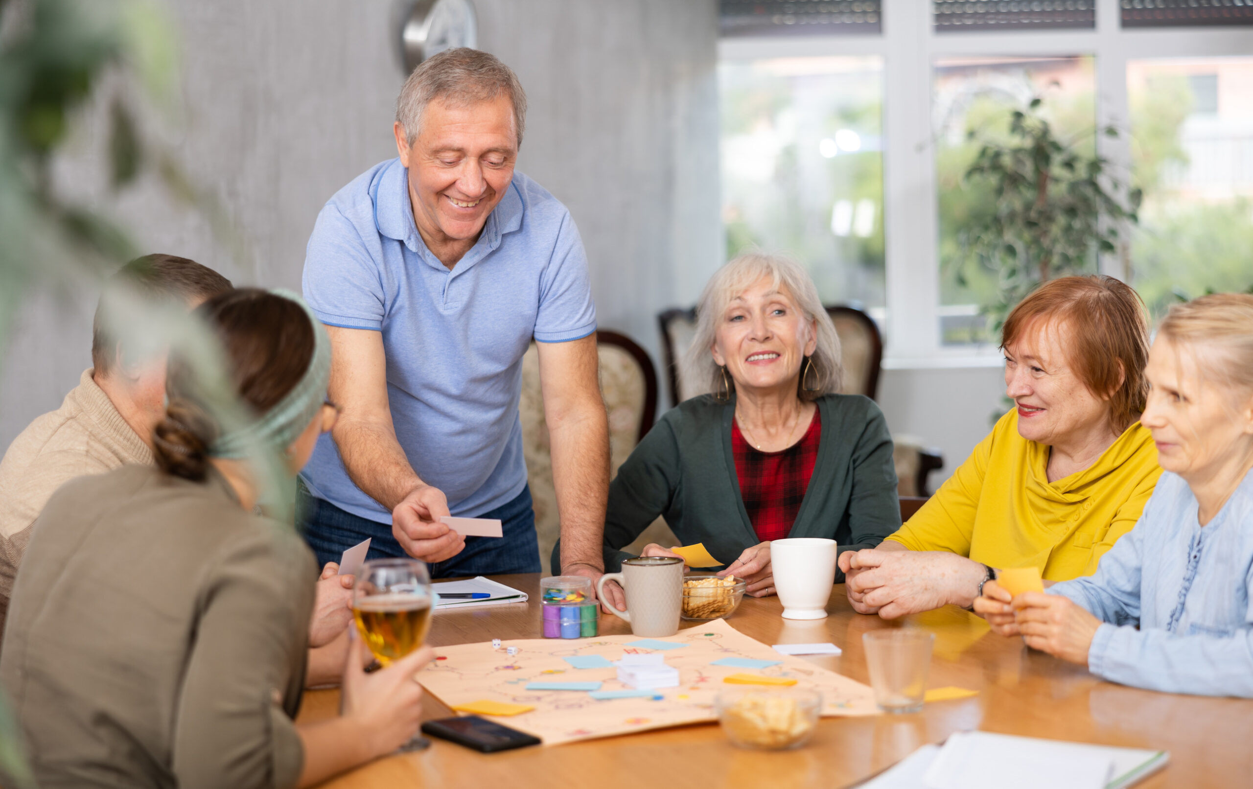 Elderly man playing board game during tea party with friends