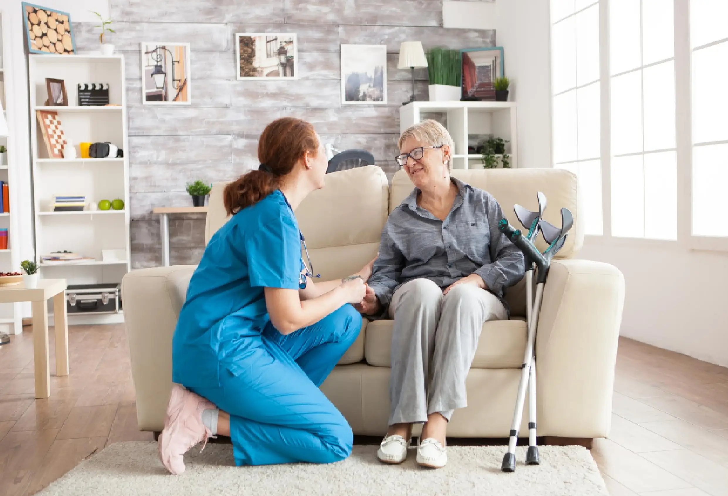 Happy old woman in a nursing home sitting on couch talking with her caretaker